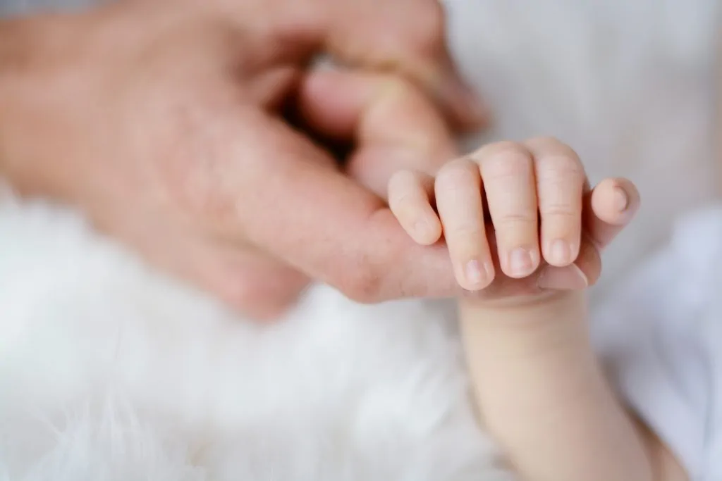 Baby holding adults finger.