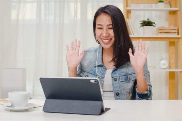 Asian woman with hands up smiling at laptop.