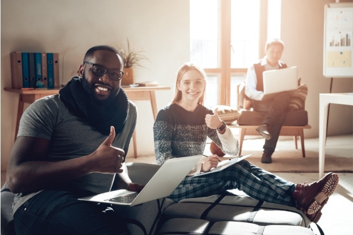 Two people smiling at camera sitting on floor with a thumbs up.