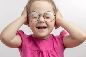 Young girl wearing glasses covering her ears.