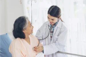 Doctor checking heart rate of an older person sitting in hospital bed.