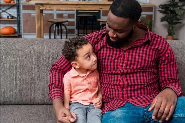 Adult sitting with their arm wrapped around a young person.