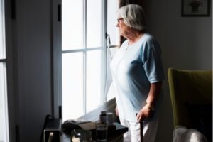 Older woman holding cane looking outside her window feeling social isolation