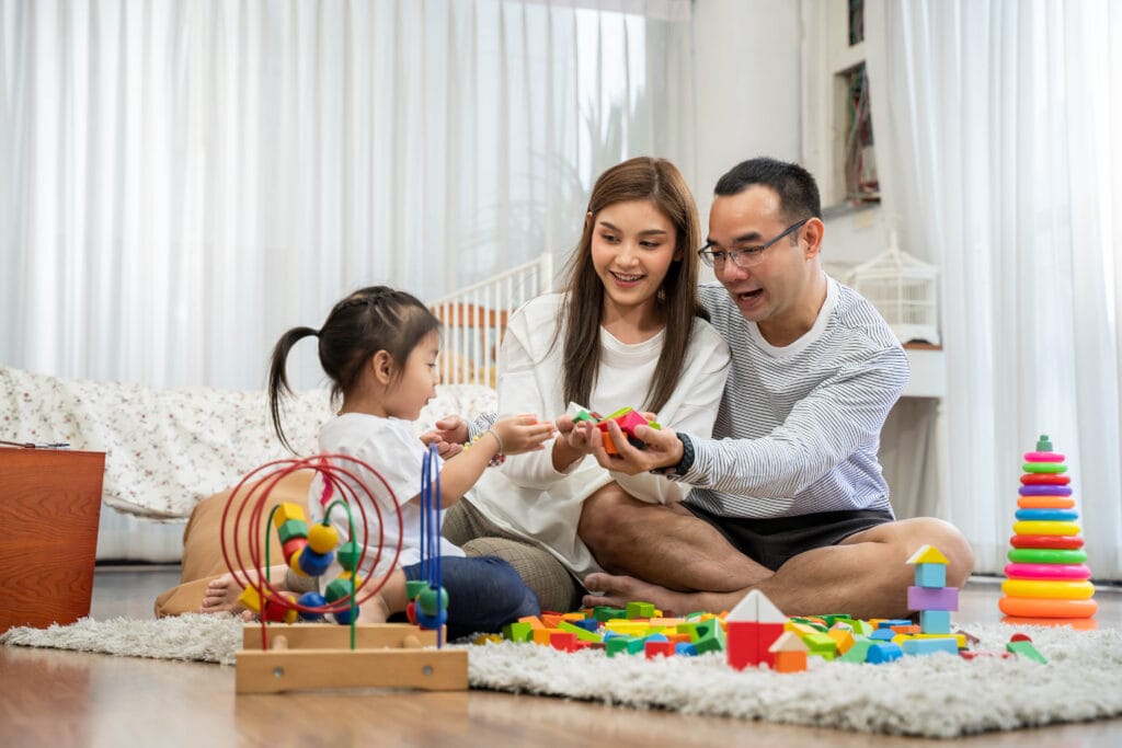 Mother and father and young daughter sitting on floor playing with toys.