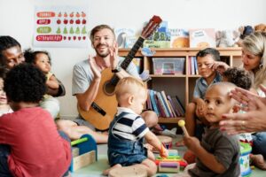 Teacher holding a guitar surrounded by a group of students.
