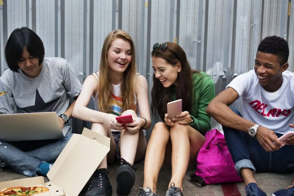 Group of students sitting on concrete floor looking at cellphones.