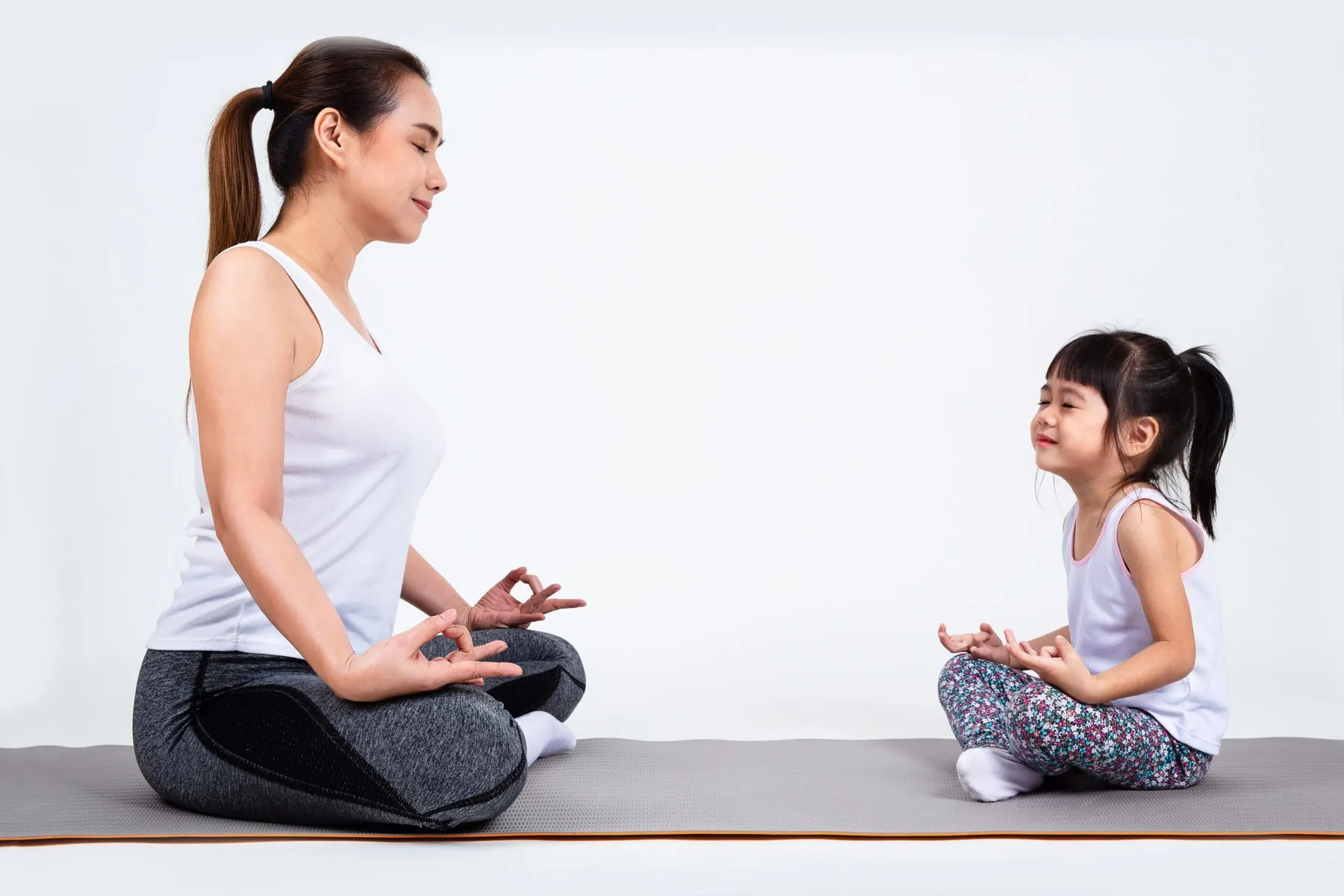 Daughter and mother sitting on yoga mat meditating.