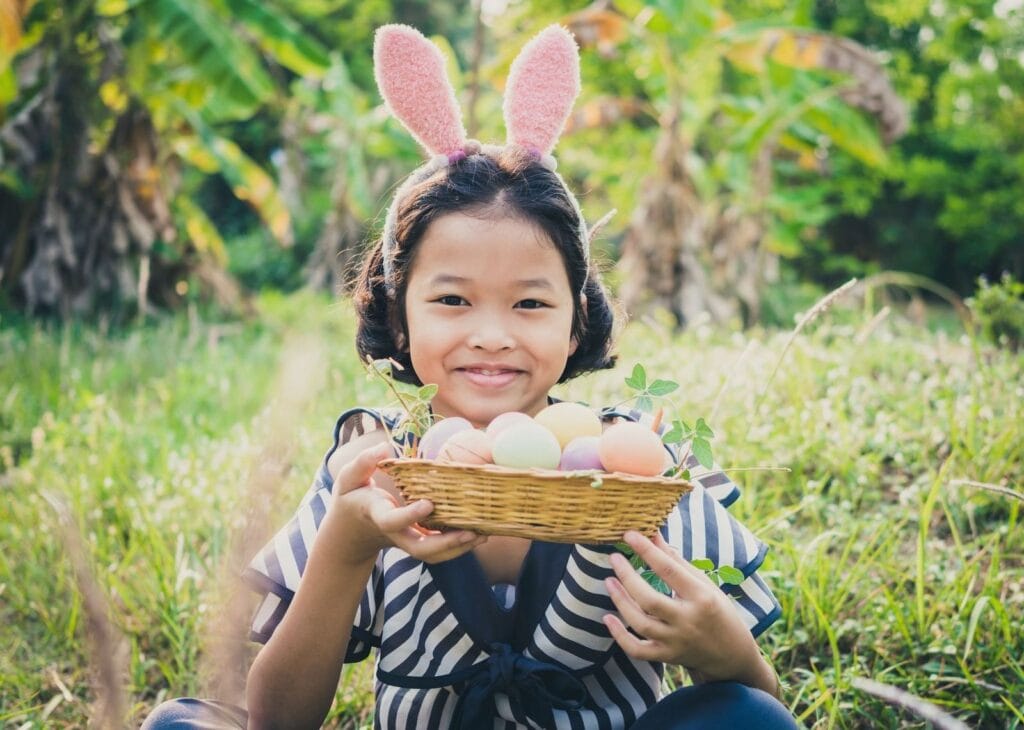 Young Asian girl wearing bunny ears holding a basket of Easter eggs.