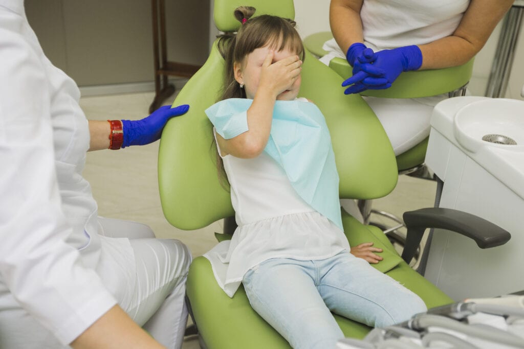 Girl in dentist chair with hand over face experiencing sensory overload.