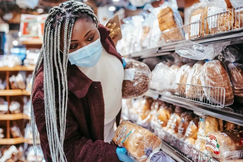 Black woman wiht long braids wears a mask while grocery shopping