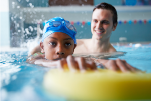 Young child and swim instructor during sensory-friendly swim lessons kicking in swimming pool..