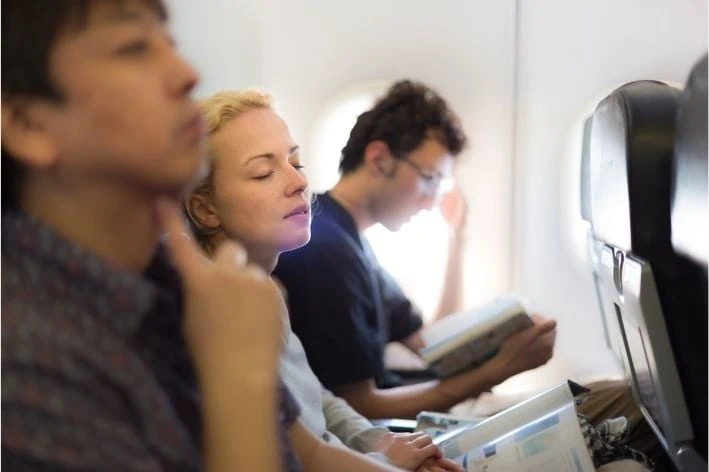 Woman sitting on plane between two passengers experiencing sensory overload.
