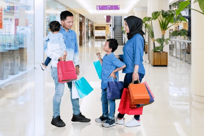 Young family standing in shopping mall holding colourful shopping bags.