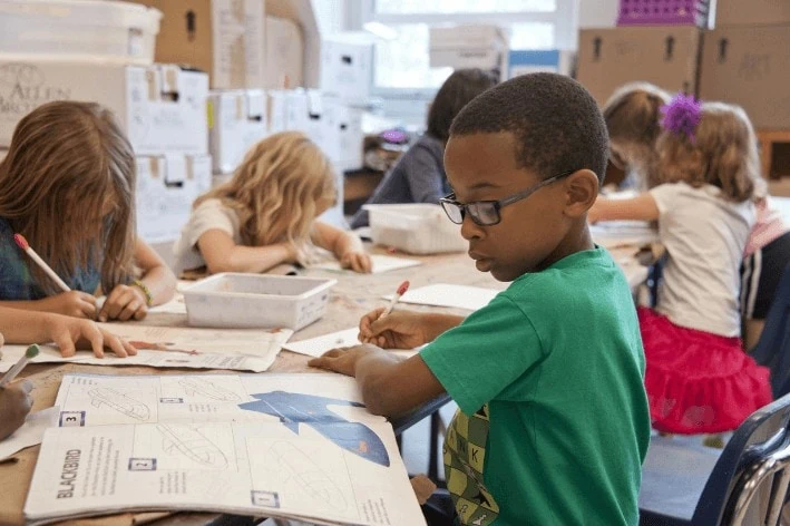 Young students at school sitting at a table completing a writing activity.