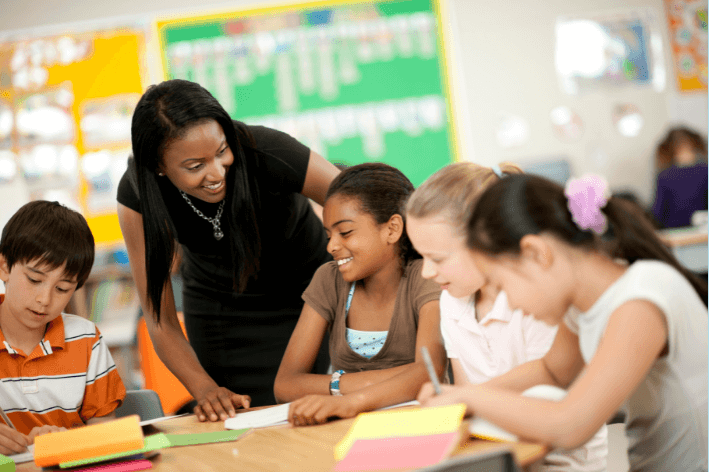 Teacher helping students sitting at a table in a classroom.