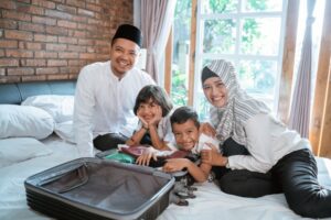 Young family sitting on hotel bed with suitcase while on a sensory-friendly vacation.