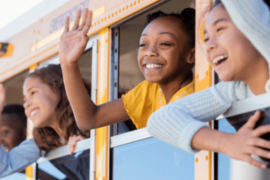 Young students smiling waving outside of school bus window.