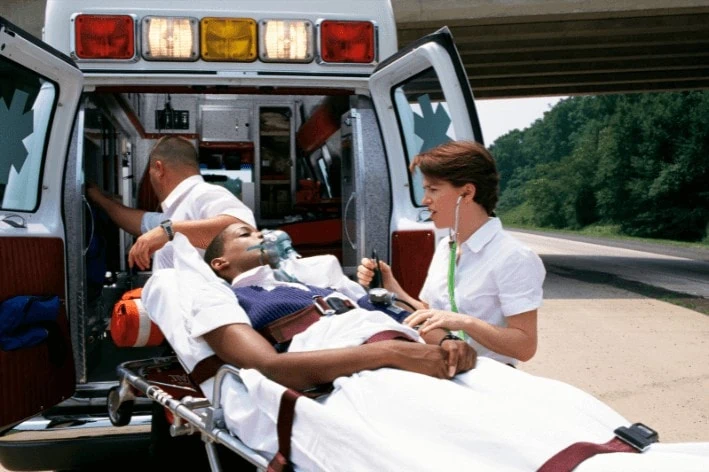 Patient being lifted into the back of an ambulance with the help of a paramedic.