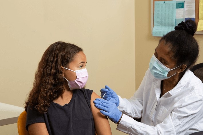 Masked doctor giving a masked young girl a vaccine at a sensory-friendly vaccination clinic.