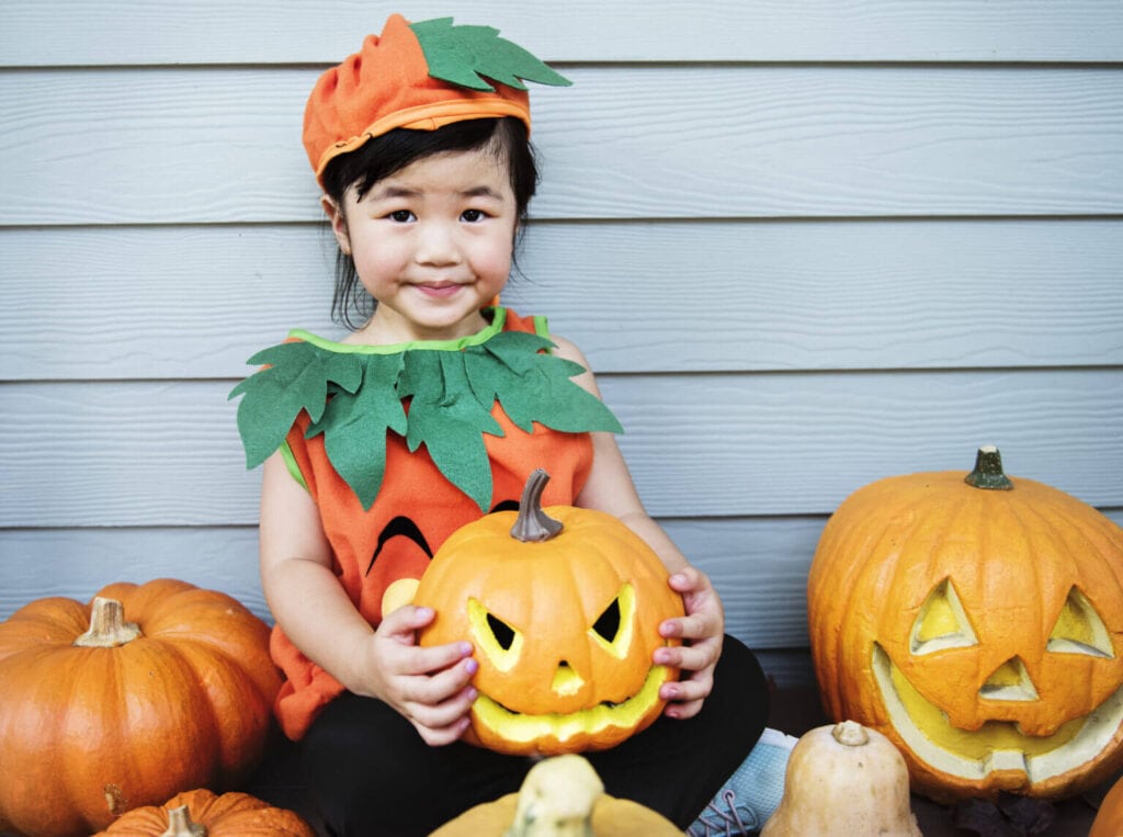 Young child dressed as a pumpkin for Halloween holding a pumpkin.