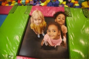 Three young girls at standing on trampoline at indoor recreation center.