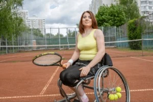 Young girl in wheelchair holding racket on tennis court.