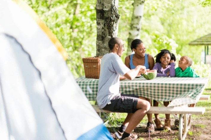 Young family sitting on picnic table at campsite eating watermelon.
