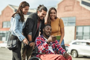 Three adults surrounding an adult sitting in a wheelchair holding a phone.
