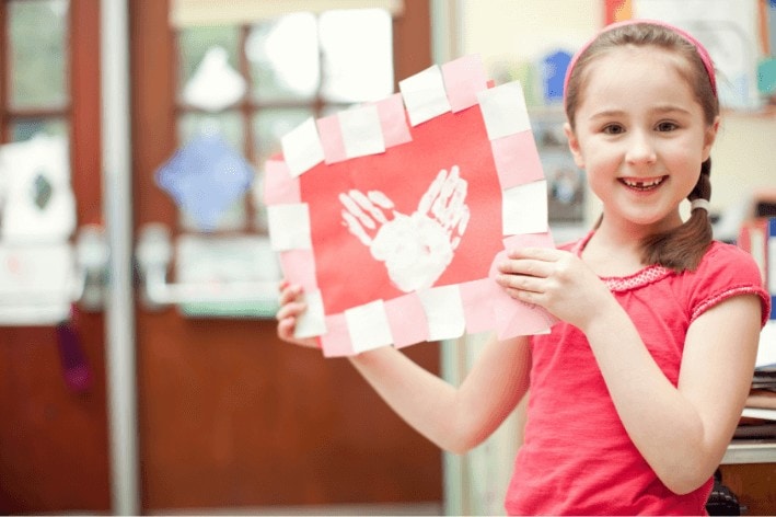 Young girl holding up Valentine's Day craft.