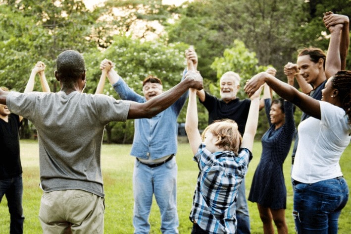 Group of people of all ages hold hands up in a circle.