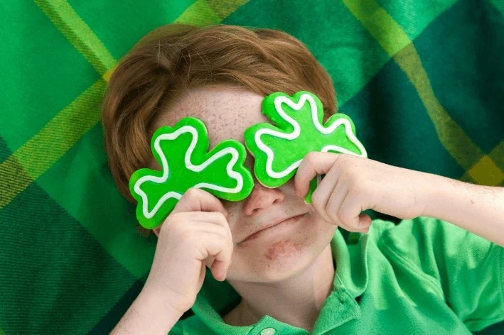Young child laying on blanket with shamrocks on their eyes on St. Patrick's Day.