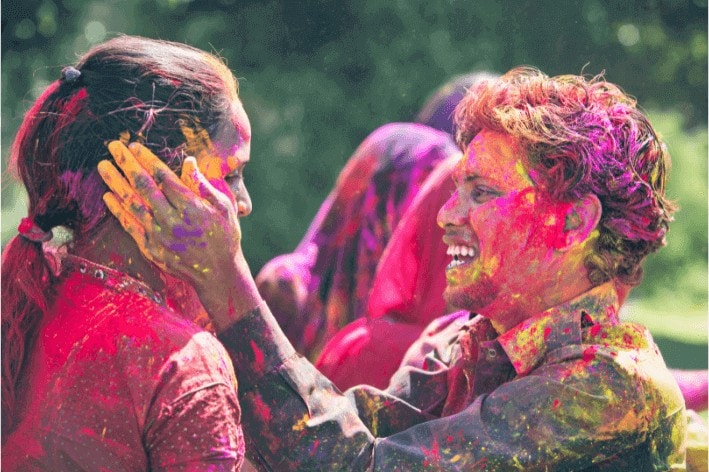 Smiling person putting colour powder on another person's cheeks during sensory-friendly Holi celebration. 