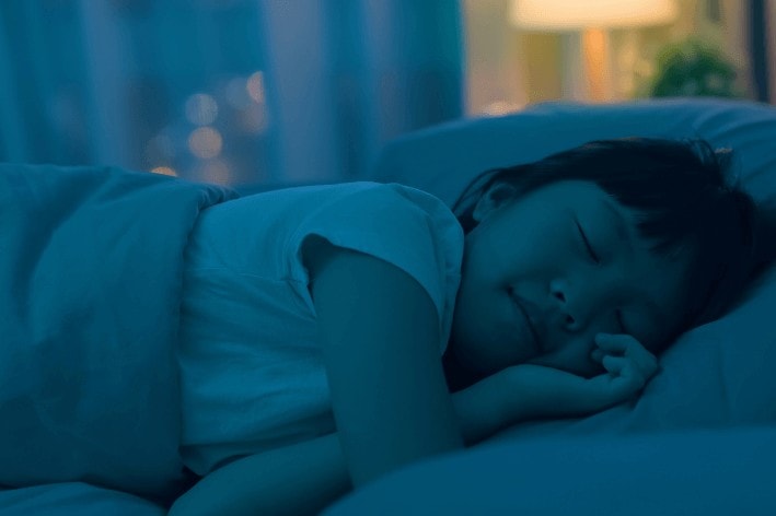 Young girl sleeping in bed in dark room.