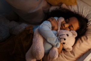 Young girl sleeping in bed holding stuffed animal.