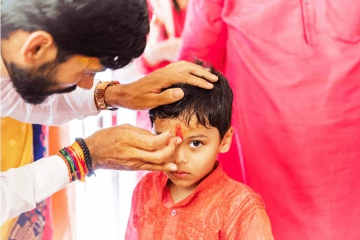 An adult putting a traditional red powder on a child's forehead for Tamil New Year.
