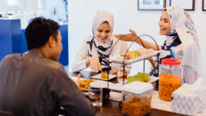 3 young Muslim adults seated around dinner table eating.