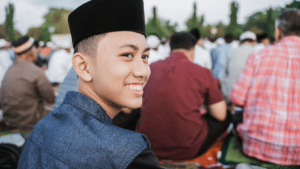 Young Muslim man, smiling, with his head turned to the side, outside in group prayer.