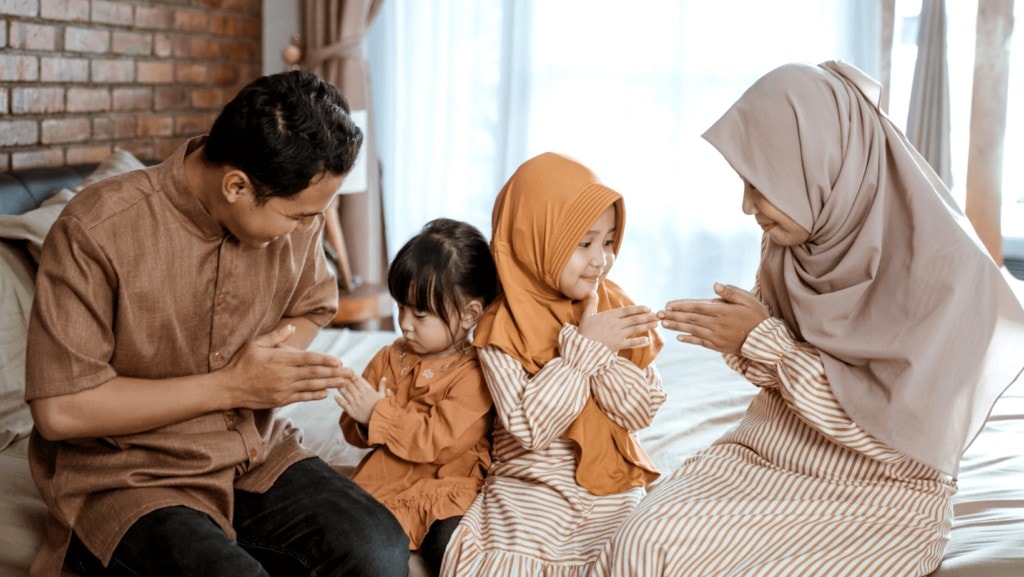 Muslim family praying together sitting on bed.