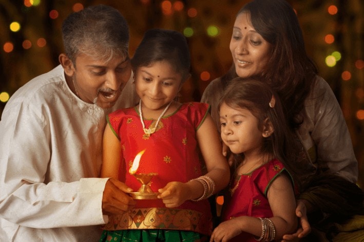 Two parents and daughters lighting an oil lamp with Indian traditional outfits on at a sensory-friendly Diwali celebration.