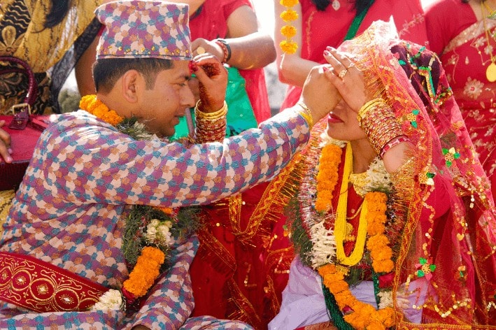 Bride and groom in their traditional outfit applying a red powder on each other's forehead.