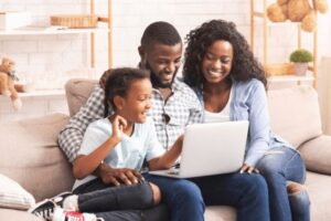 Family of three sitting on a couch and watching a sensory-friendly show online on a laptop.