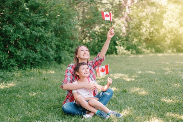Mother and child sitting on lawn holding Canadian flags.