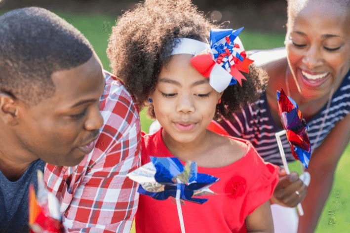 Parents and child dressed for Independence Day blowing windmills.