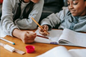 Young girl holding pencil completing homework with mother helping her.