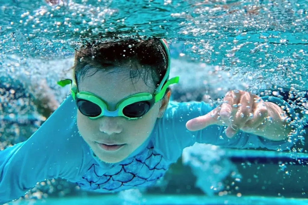 young boy swimming underwater with froggles brand goggles and blue swim shirt