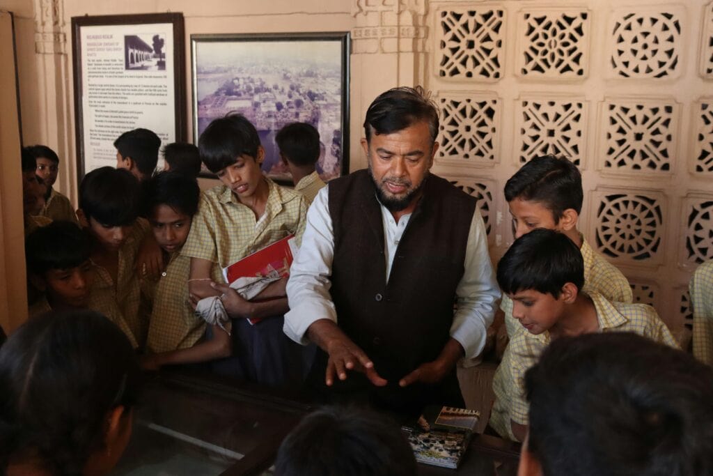 a guide with a group of children at  museum exhibit