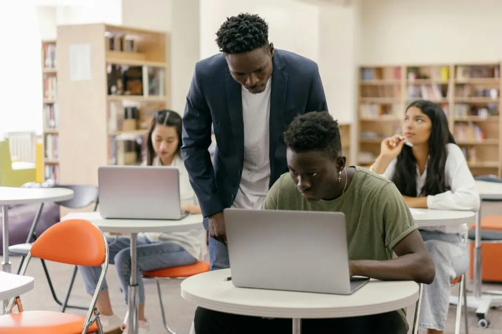 A teacher looking over a students sholder in a college classroom