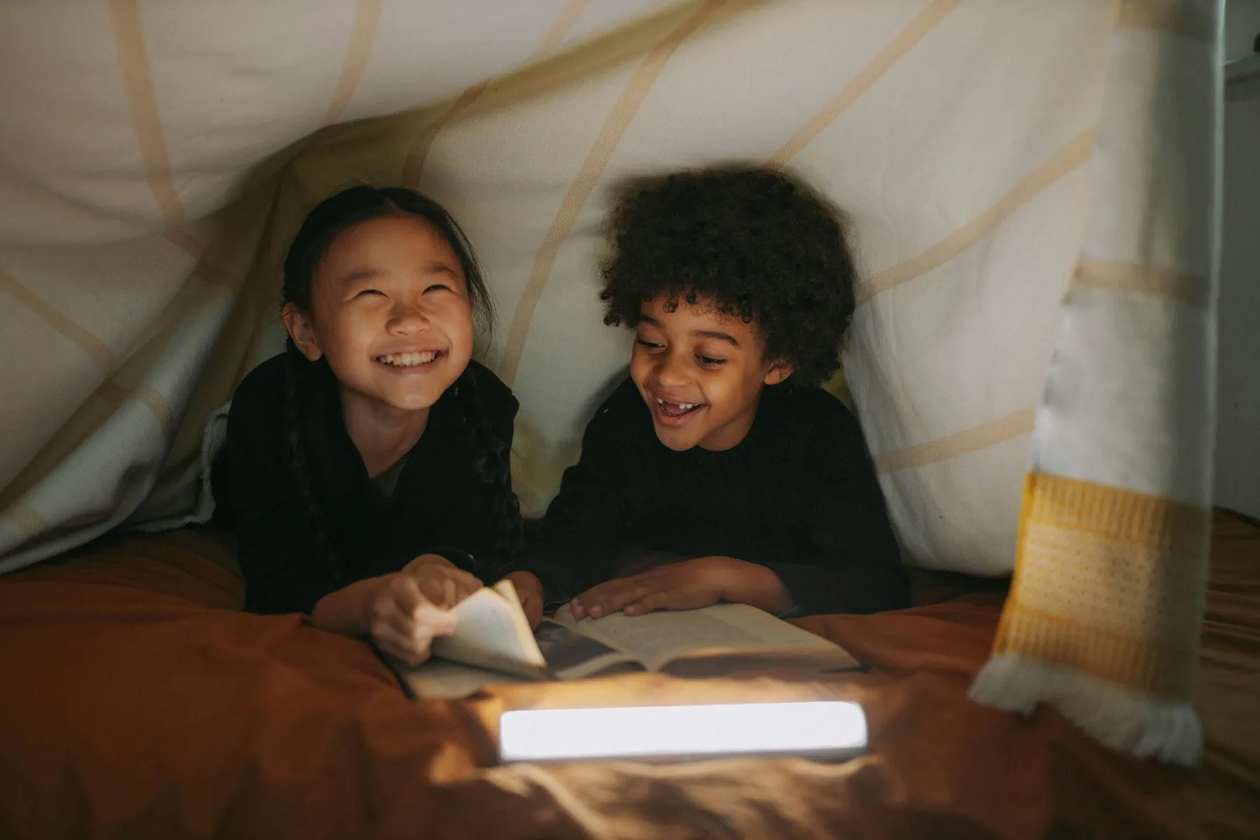 two children, laughing, reading, in a tent