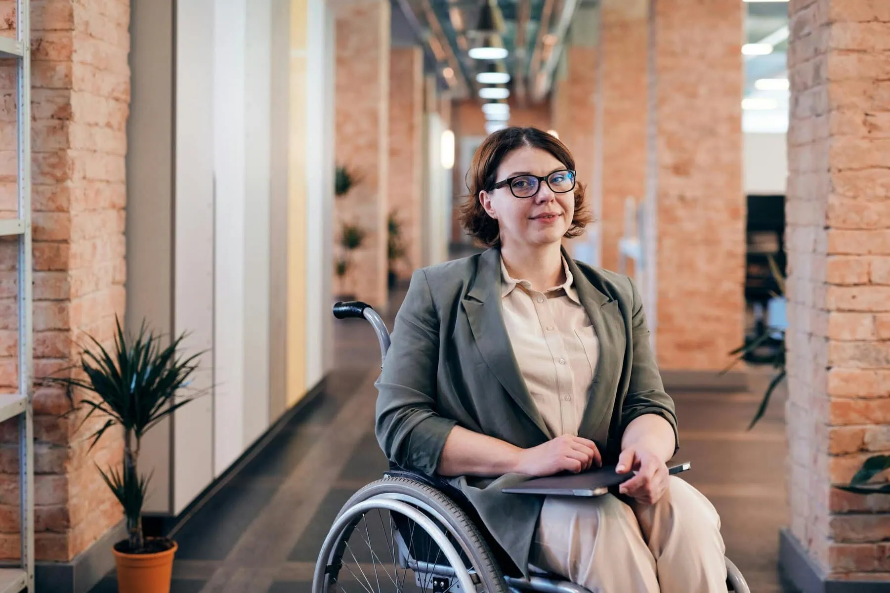 woman wearing glasses, sitting in a wheelchair, with a laptop on her lap in a conference hall